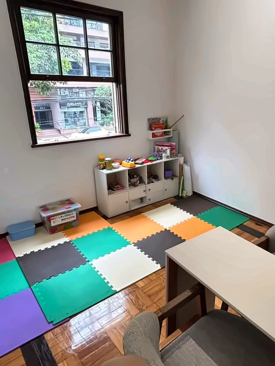 Sala de atendimento infantil com piso colorido, brinquedos e livros.