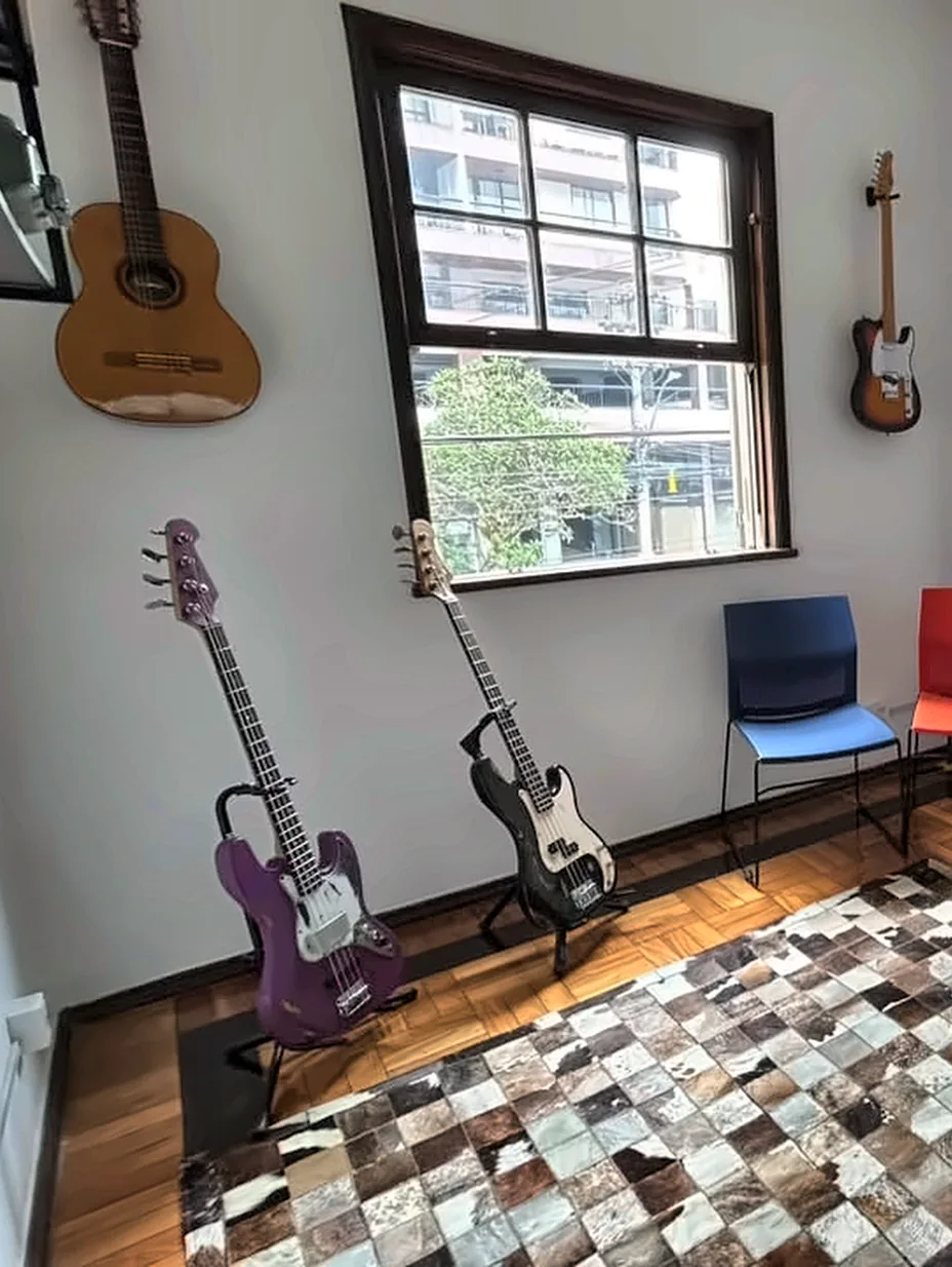 Sala de música com violão, guitarras e janela para a rua.