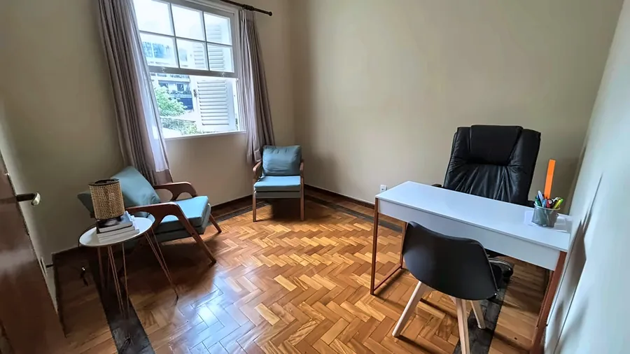 Sala de atendimento adulto vista da porta, com poltronas, mesa e janela.