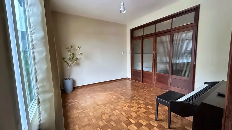 Sala coletiva com piso de taco, planta, piano e portas de madeira e vidro.