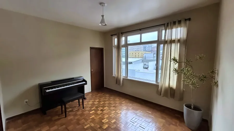 Sala coletiva com piano e janela com cortinas claras.