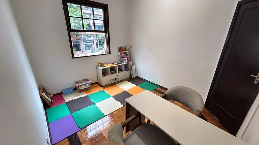 Sala de atendimento infantil com piso colorido, estante de brinquedos e mesa.