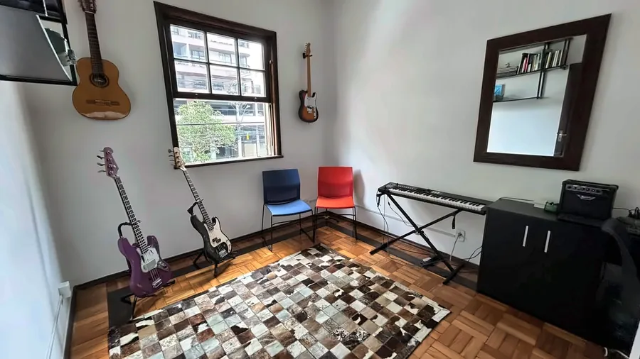 Sala de música com violão e guitarras na parede, cadeiras, teclado e tapete.