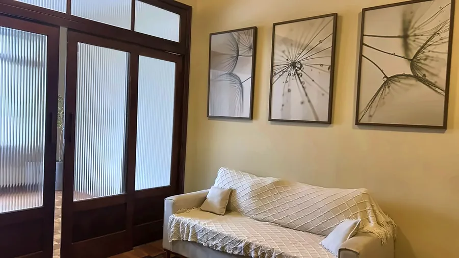 Recepção com sofá claro, almofadas e três quadros botânicos.