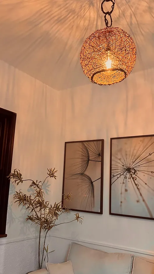 Recepção ao entardecer, com a luminária de fibras acesa sobre os quadros e o sofá.