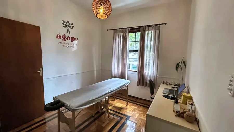 Sala de terapia integrativa com maca, luminária e a marca do Ágape na parede.